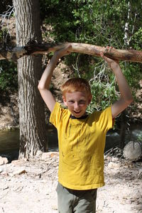 Portrait of smiling boy holding branch at forest