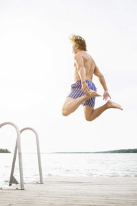 Full length rear view of man diving into lake against clear sky