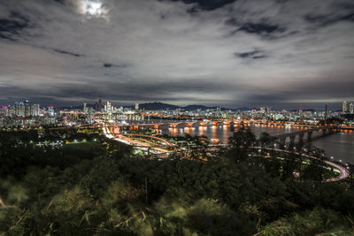 Illuminated buildings by river against sky at night