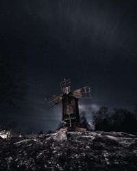 Traditional windmill on snow covered landscape against sky at night