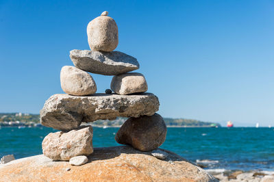 Stack of rocks in sea against clear blue sky