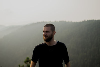 Young man looking away against sky