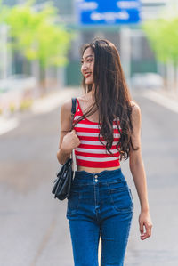 Smiling woman with sling bag walking on street