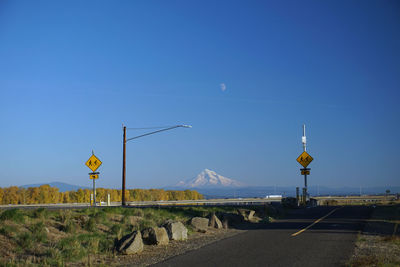 Road sign against clear blue sky with mountain in background