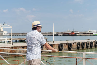 Summer travel. male tourist in straw hat walking in the sea port, boats and yachts on the background