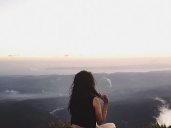 Rear view of woman photographing against sky during sunset