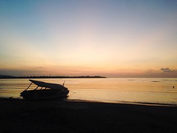 Boat moored on beach against sky during sunset