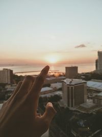 Hand of person pointing at sun during sunset