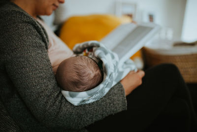 Midsection of mother with baby boy reading book while sitting at home