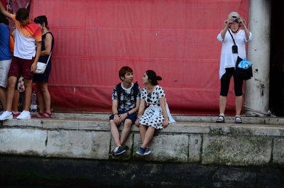 Rear view of people sitting on wall