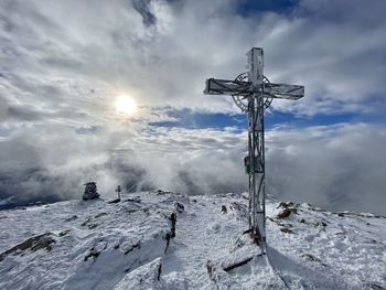 View of cross on snow covered land against sky