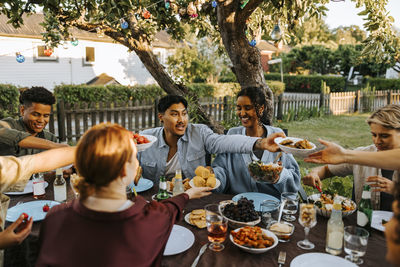 Male and female friends passing food to each other while having dinner in back yard at social gathering
