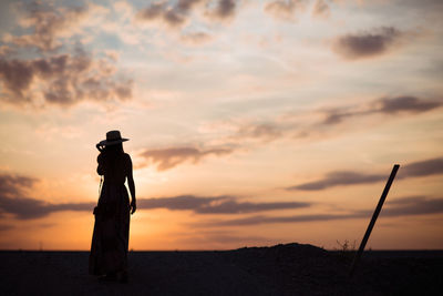 Rear view of silhouette woman standing on land against sky during sunset