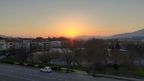 Cars on road by buildings against sky during sunset