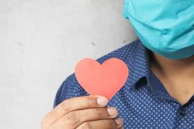 Midsection of man with mask holding heart shape leaf against wall