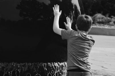 Rear view of boy pushing on built structure at fountain