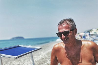 Happy shirtless senior man wearing sunglasses at beach during summer