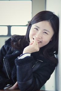 Portrait of smiling woman with hand on chin leaning against wall