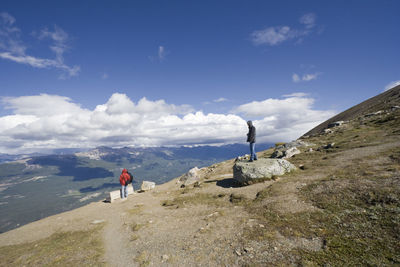 People standing on rocky mountain against cloudy sky at jasper national park