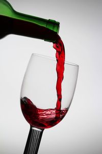 Close-up of bottle pouring red wine in glass against white background