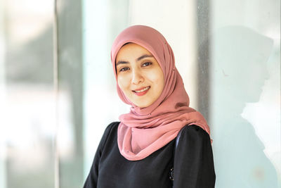 Portrait of smiling young woman standing against wall