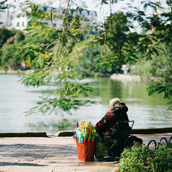 Rear view of woman sitting on chair by lake