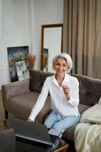 Positive woman entrepreneur sitting on armchair while working on laptop