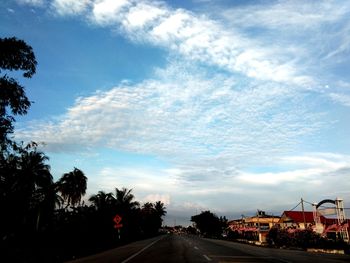 Road by silhouette trees against sky in city