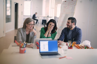 Creative business people smiling while discussing over laptop at desk in office