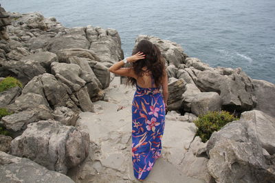 Rear view of woman walking on rocky coastline