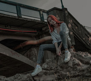 Full length of woman sitting on rock against abandoned structure