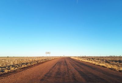 Road amidst field against clear blue sky