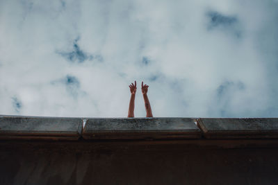 Midsection of woman with arms raised against cloudy sky