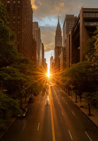 Road amidst buildings against sky during sunset