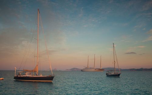Sailboats sailing on sea against sky during sunset