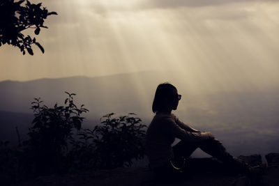 Silhouette woman sitting on mountain against sky during sunset