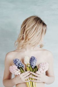 Shirtless woman holding flowers against wall