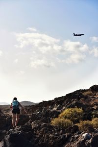 Rear view of helicopter flying over rocks against sky