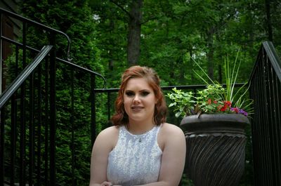 Portrait of young woman sitting by railing in forest