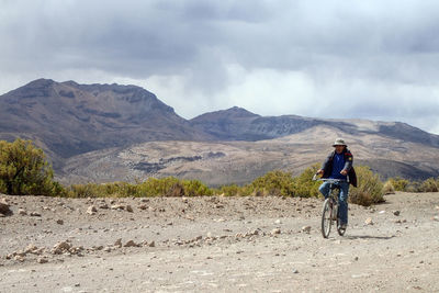 Man riding bicycle on dirt road against sky