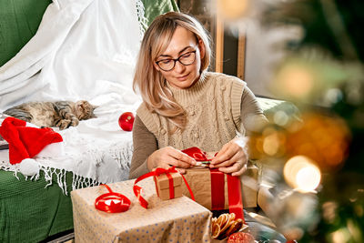 Blond woman wrapping presents in recycled card and decorated it with dried oranges and fir branches.