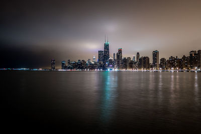 Illuminated cityscape by lake michigan against sky at night