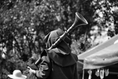 Rear view of woman carrying musical equipment while standing against trees