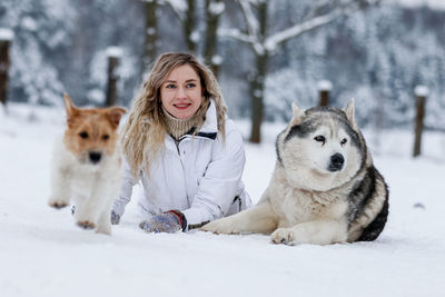 Smiling woman with dogs sitting on snow during winter