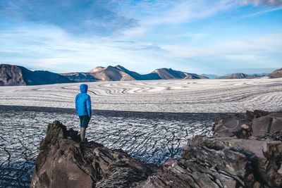 Rear view of man standing on rock against sky