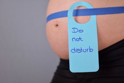 Do not disturb tag on pregnant woman abdomen standing against gray background