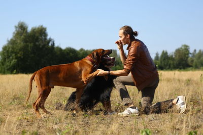 Man playing with dogs while standing on grassy land against sky