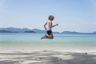 Woman jumping on beach against sky