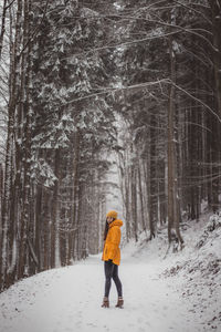 Side view of woman standing on snow covered land in forest