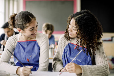 Smiling female teenage students talking during art class at high school